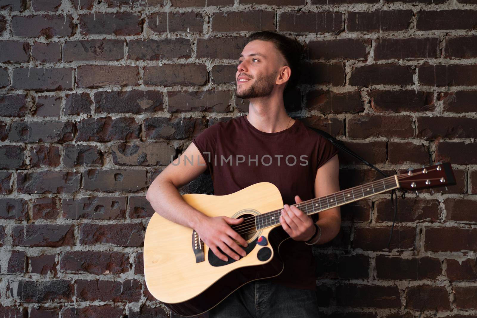 Man with acoustic guitar against brick wall playing music singing songs enjoy life Handsome caucasian male guitar player practice play musical instrument home loft interior Creative lifestyle hobby