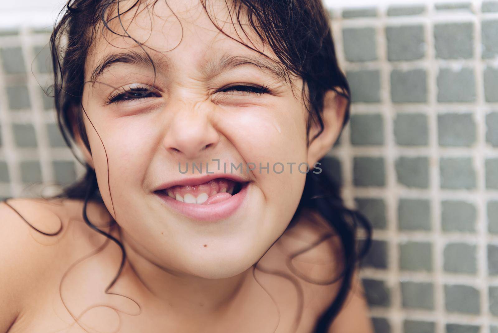 portrait of a happy pretty little girl grimacing while taking a bath in the bathtub, kids hygiene concept