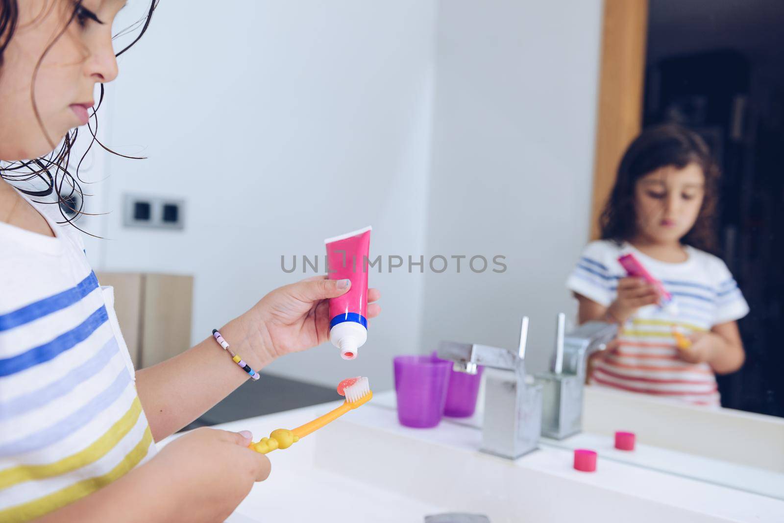 little girl putting toothpaste on the brush, after taking a shower she prepares to brush her teeth in front of the mirror of the bathroom, kids hygiene concept