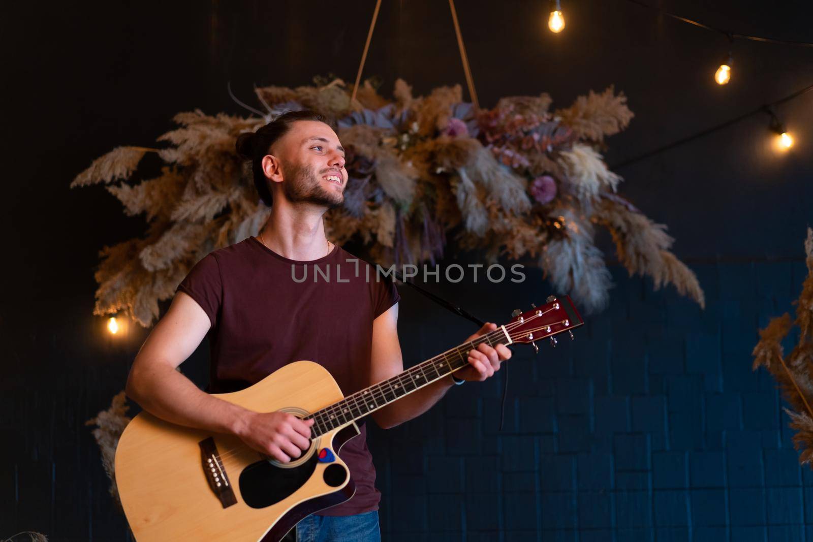 Male musician playing acoustic guitar. Guitarist plays classical guitar on stage in concert Handsome young hipster male guitar player perform private party Stylish long hair Medium shoot