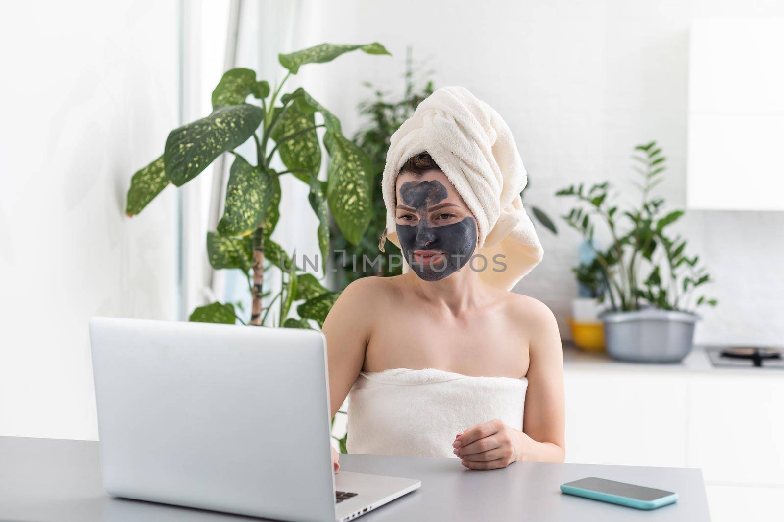 Mid adult woman in clay facial mask wearing bath towel using her laptop