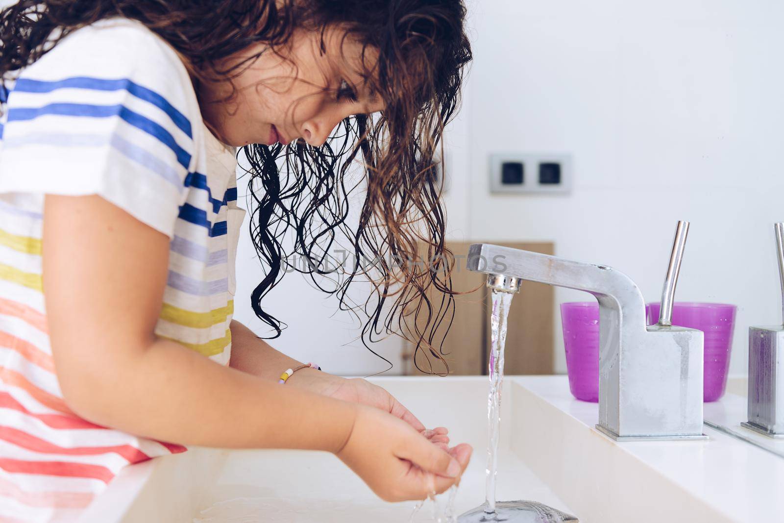little girl taking water to wash her face in the bathroom at morning after shower, kids hygiene concept
