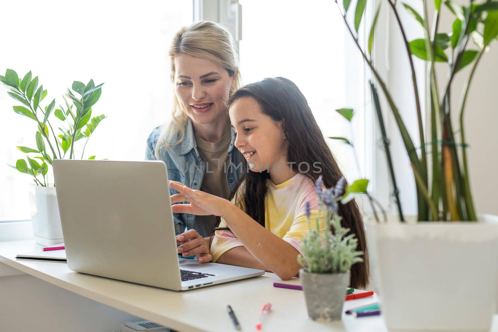 Happy mother with little kid daughter having fun online with application, watching video cartoons or playing game on laptop together, young babysitter or nanny teaching child girl to use computer.