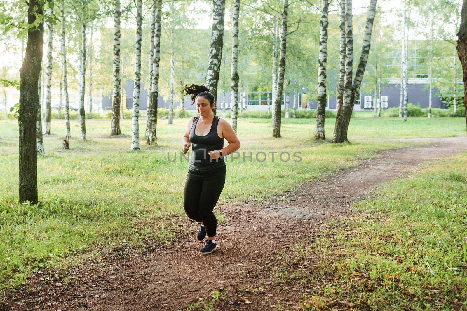 A charming brunette woman plus-size body positive practices sports in nature.