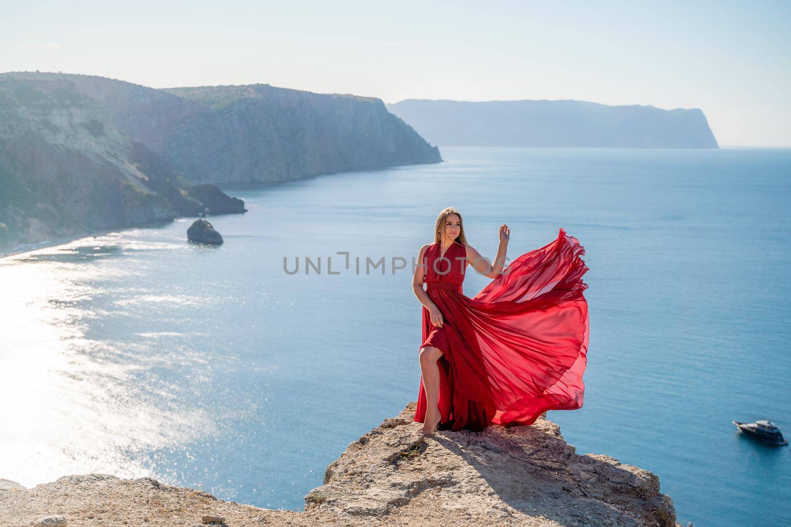 A woman in a red flying dress fluttering in the wind, against the backdrop of the sea