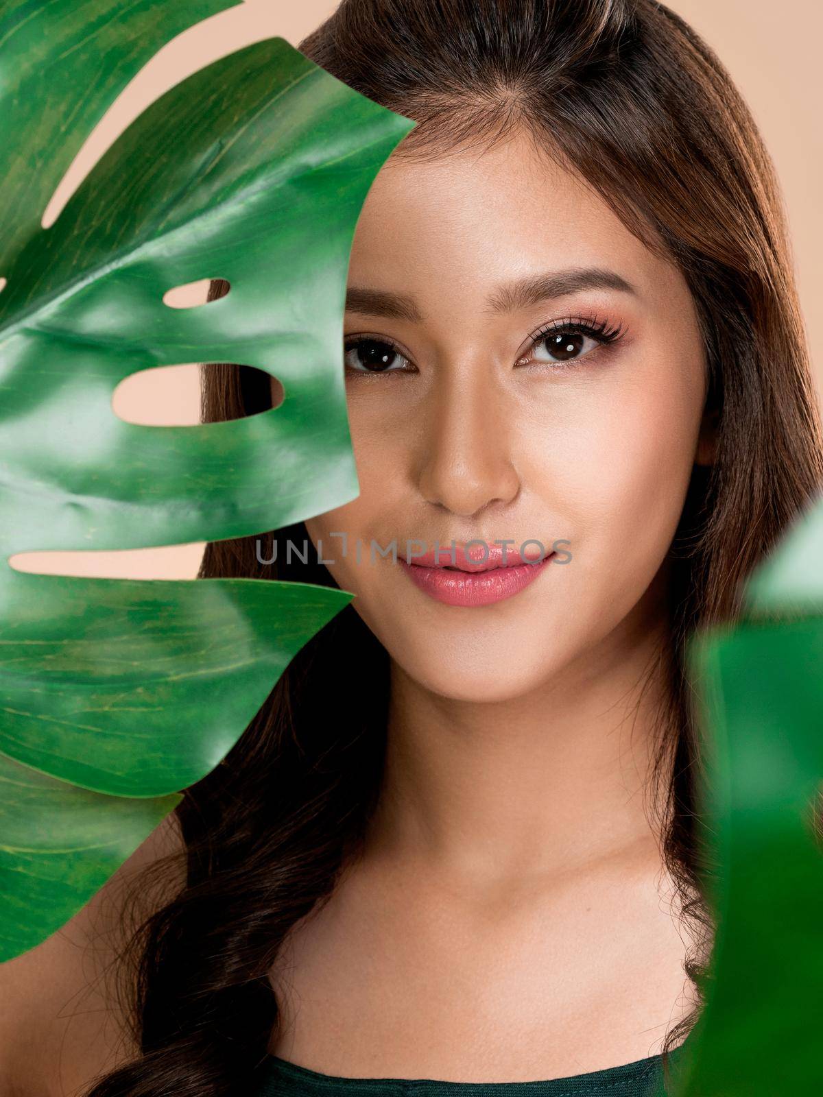 Closeup portrait of young ardent woman with healthy fair skin holding big green leaf near her face. Skin care beauty care concept.