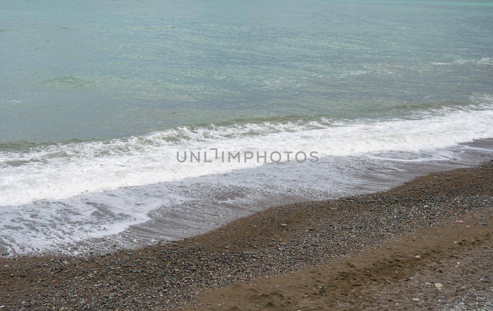 Sea shore with pebbles, wet sea pebbles on the beach and quiet sea surf. Restless sea and waves
