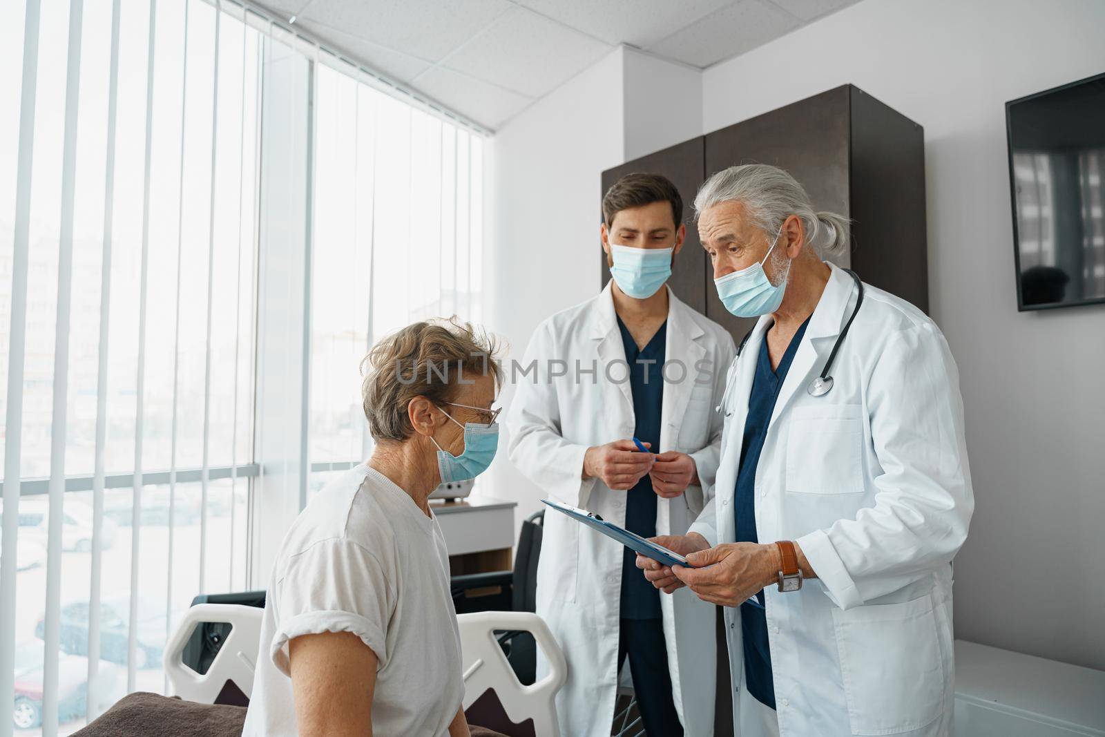 Doctors in masks explain to a sick patient in a wheelchair her diagnosis . High quality photo