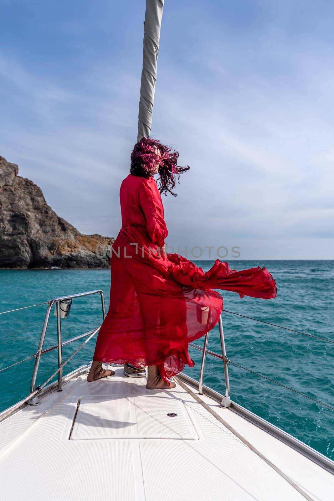 Attractive middle-aged woman in a red dress on a yacht on a summer day. Luxury summer adventure, outdoor activities