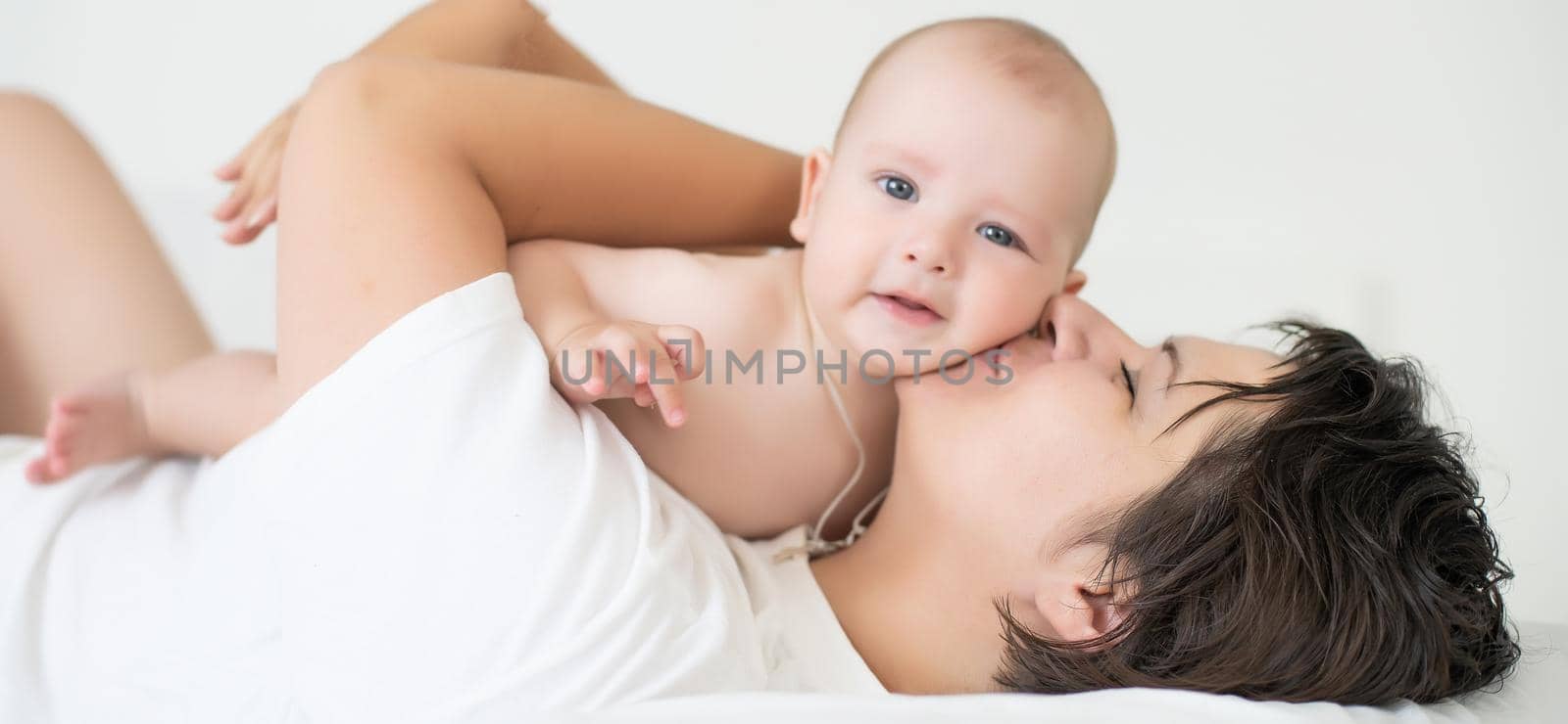 happy family. Mother and baby playing and smiling on bed by Andelov13