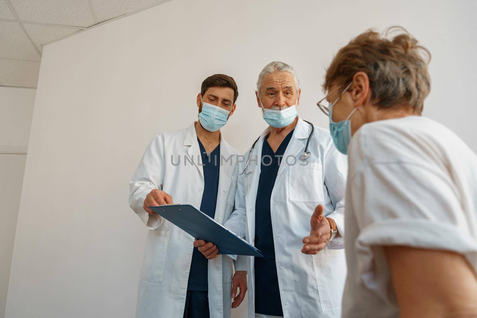 Doctors in masks explain to a sick patient in a wheelchair her diagnosis . High quality photo