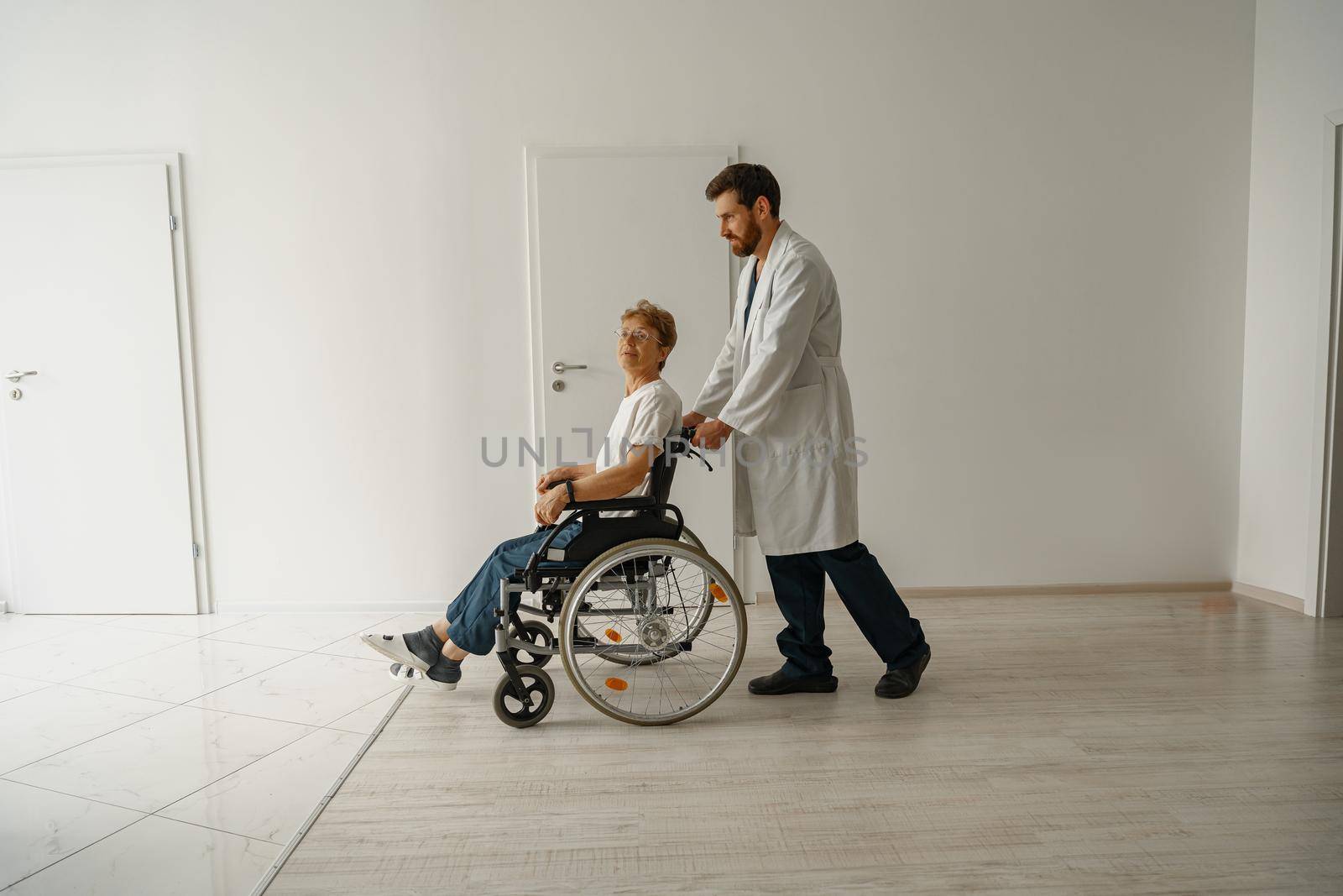 Professional male doctor carrying patient on wheelchair in medicine clinic hall. High quality photo