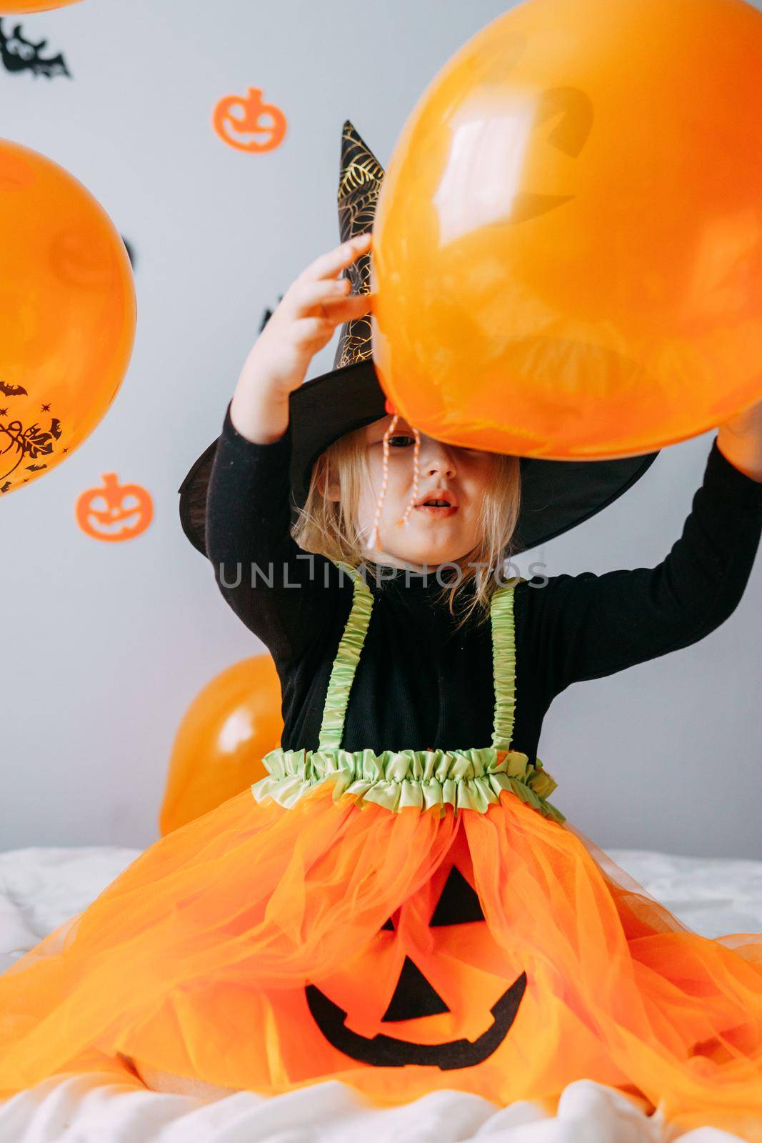 Children's Halloween - a girl in a witch hat and a carnival costume with airy orange and black balloons at home. Ready to celebrate Halloween by Annu1tochka