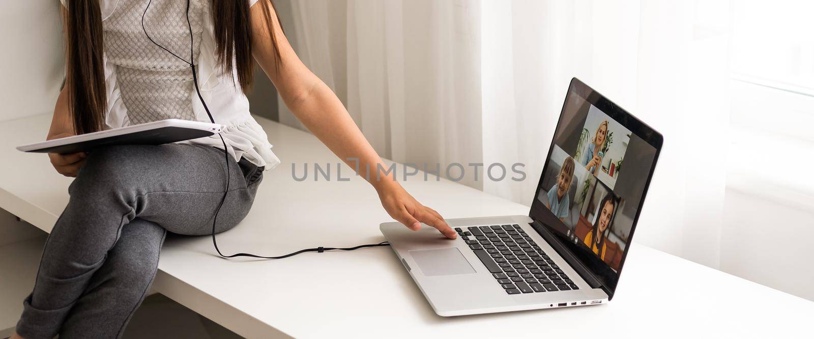 Closeup photo of little pretty pupil school lady talk skype notebook online lesson video call sit desk use earphones distance greet classmates wave arm quarantine study living room indoors