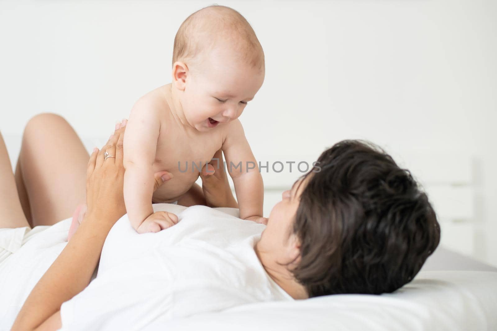 happy family. Mother and baby playing and smiling on bed by Andelov13