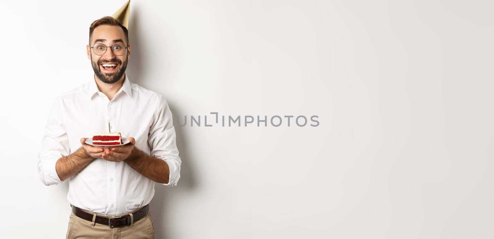 Holidays and celebration. Happy man having birthday party, making wish on b-day cake and smiling, standing against white background by Benzoix