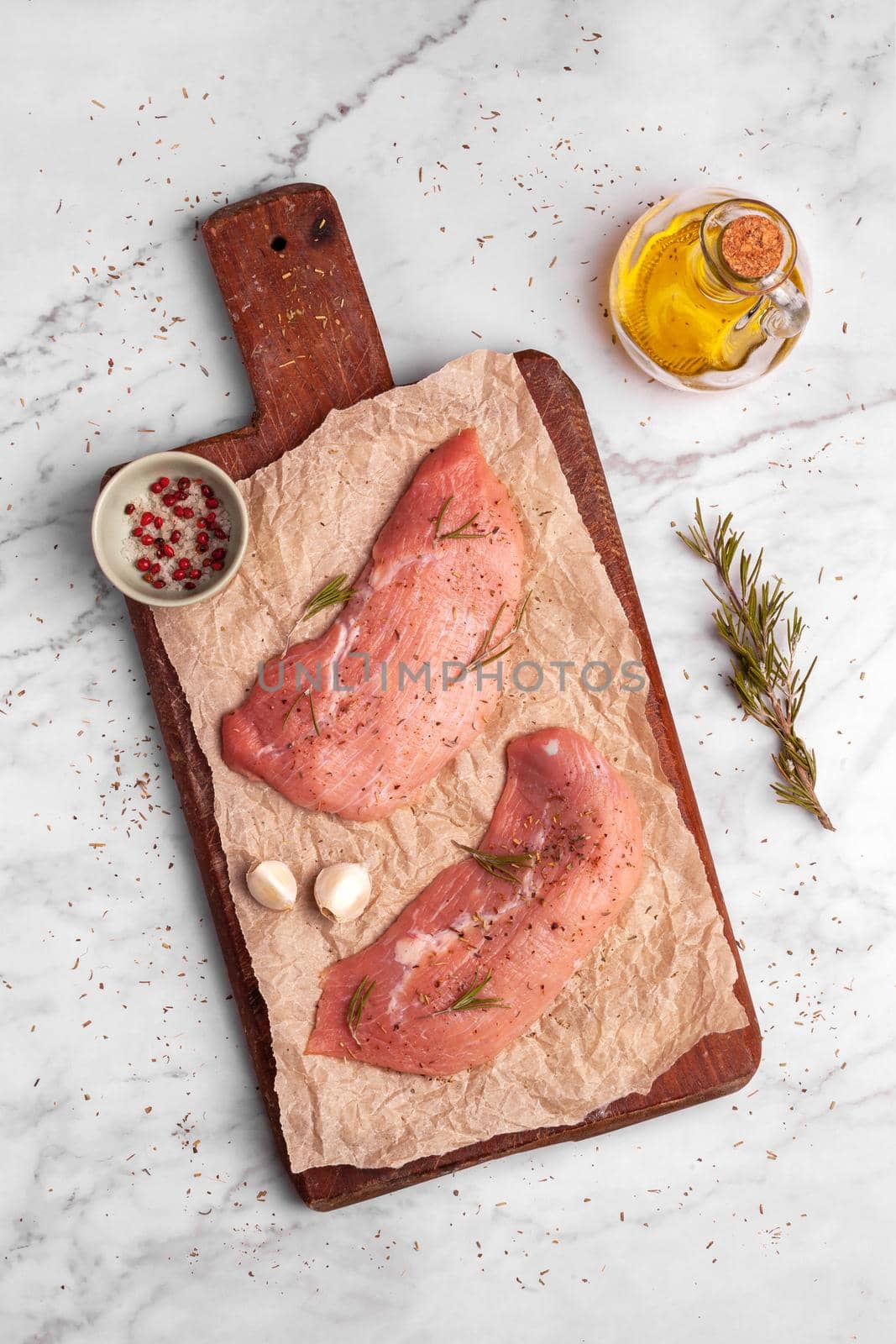 two raw veal escalope on the old wooden cutting board, ready to cook, marbre background, top view,