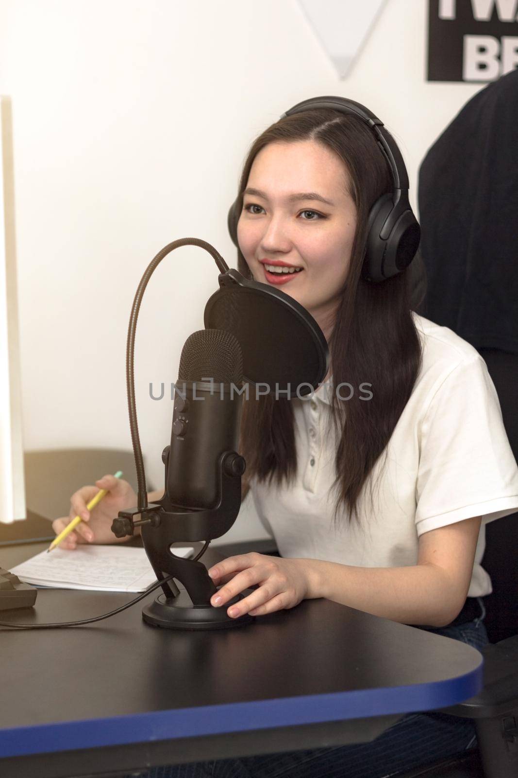 Young smiling woman with microphone and headphones recording podcast at studio, professional record audio, technology and media concept, vertical image