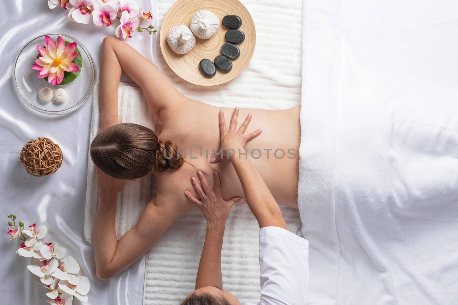 Woman at spa thai massage tow view, beauty treatments concept. Orchid and lotus flowers coconut stones and herb pouches