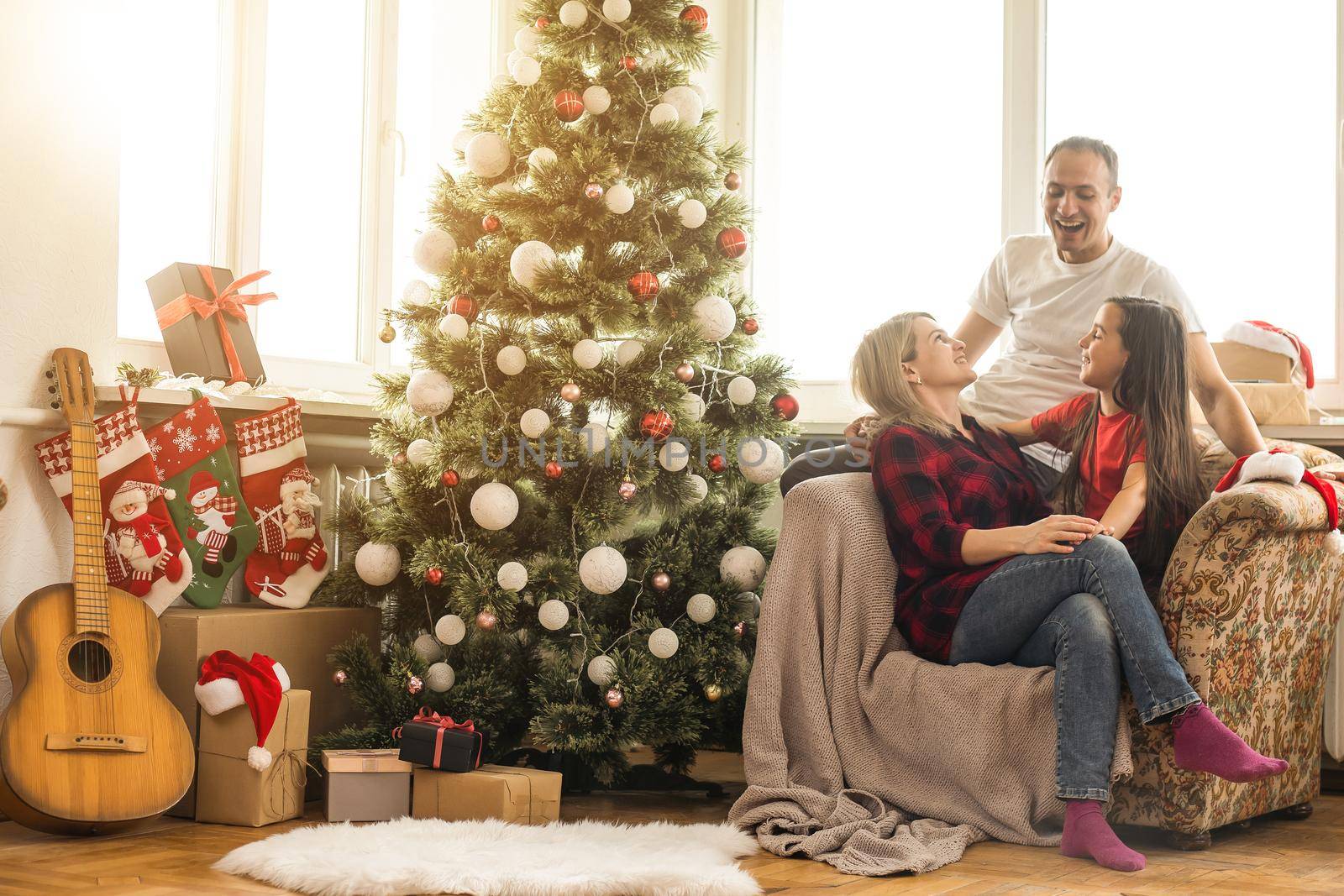 Merry Christmas and Happy New Year. Happy family is waiting for the New Year while sitting near beautiful Christmas tree at home by Andelov13