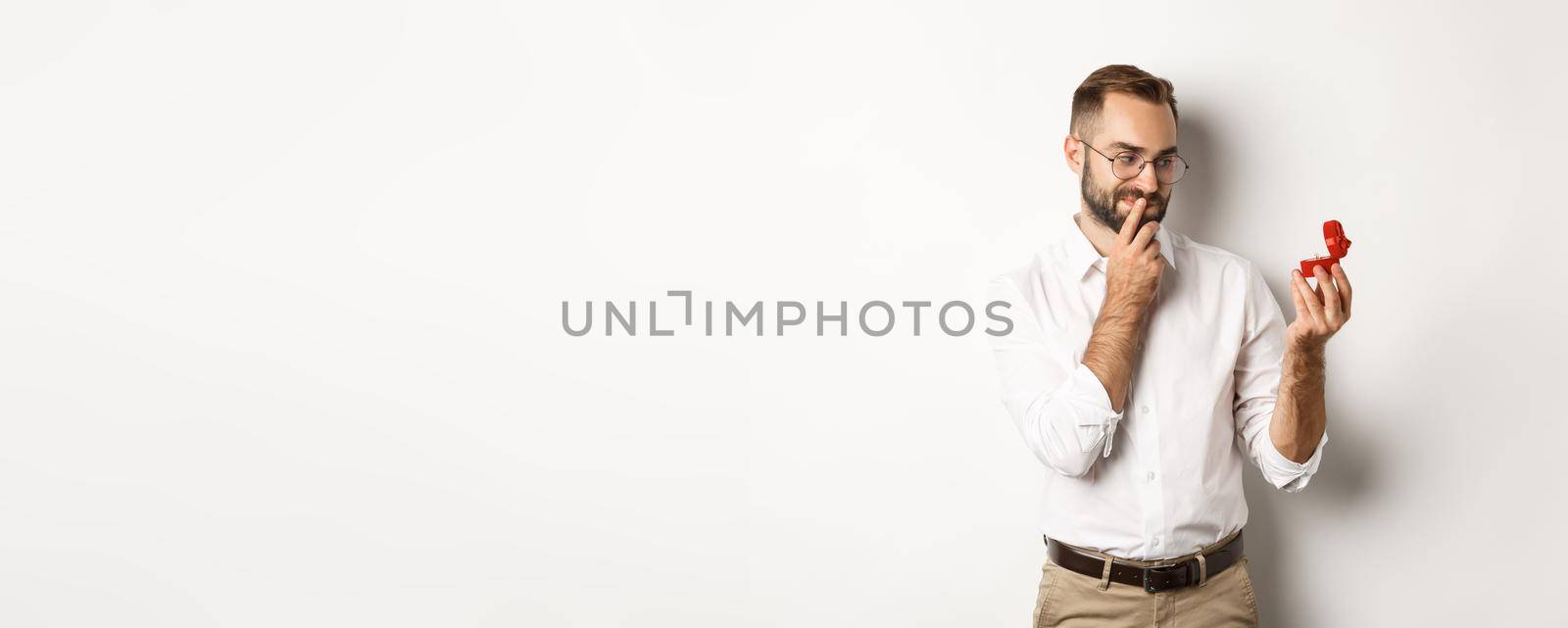 Happy man looking thoughtful at wedding ring in box, thinking about marriage proposal by Benzoix