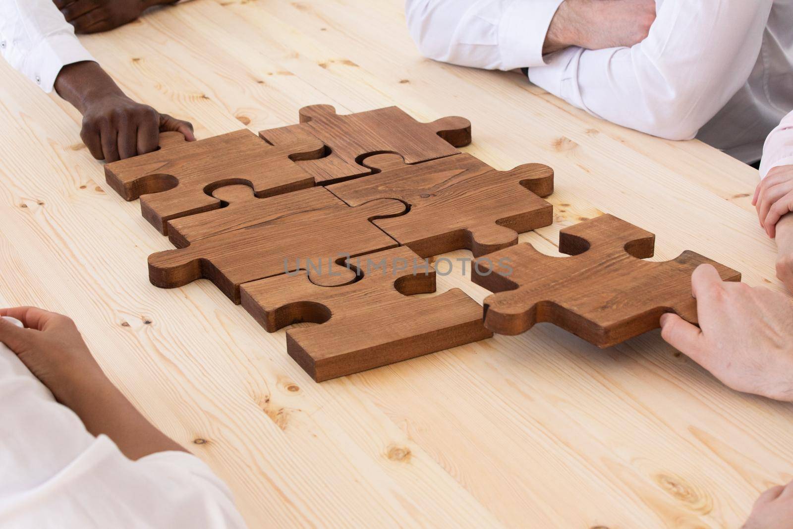 Business people team sitting around meeting table and assembling wooden jigsaw puzzle pieces unity cooperation ideas concept