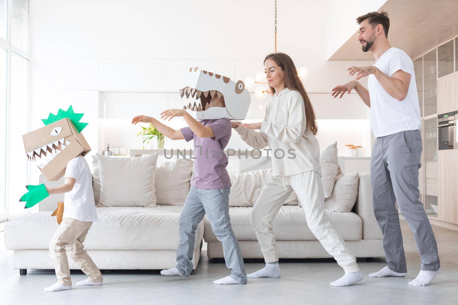 Happy family of parents and two children playing dinosaurs at home, children wearing handmade costume mask of cardboard