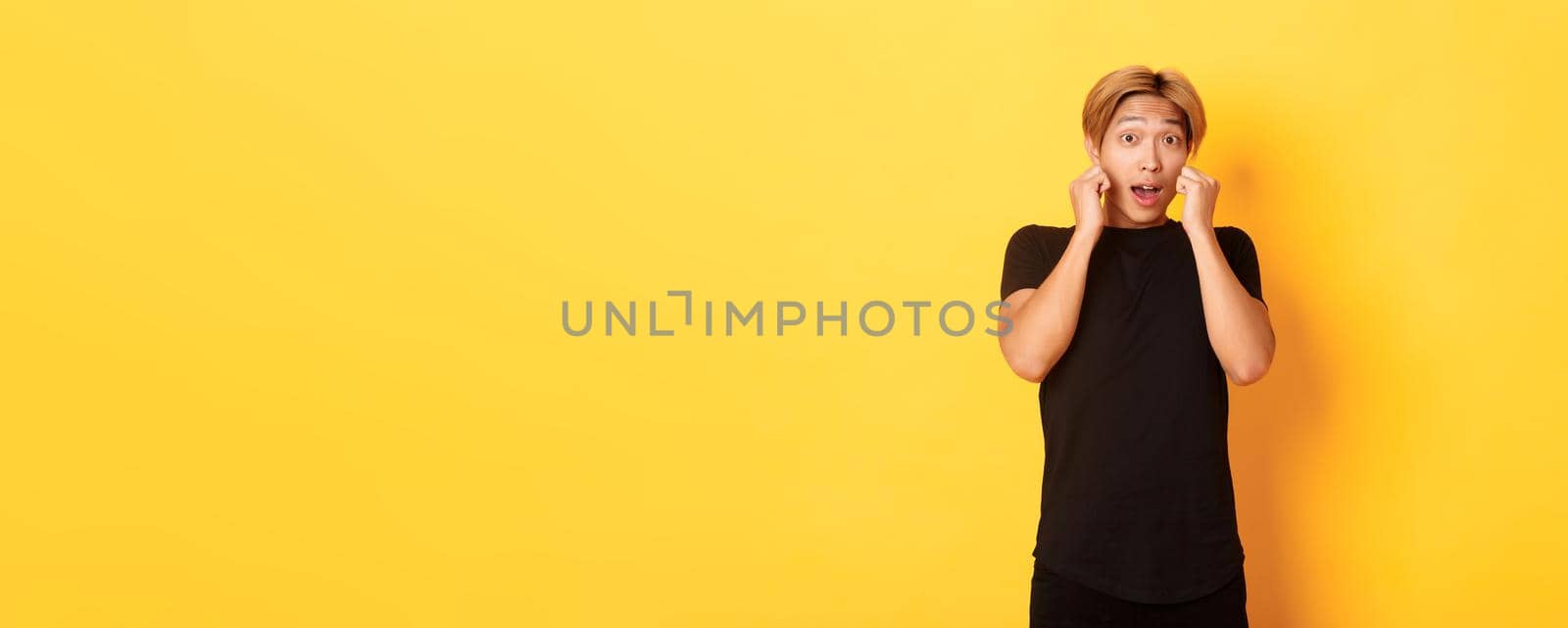 Excited handsome blond guy in black clothes, looking tempted and standing over yellow background by Benzoix