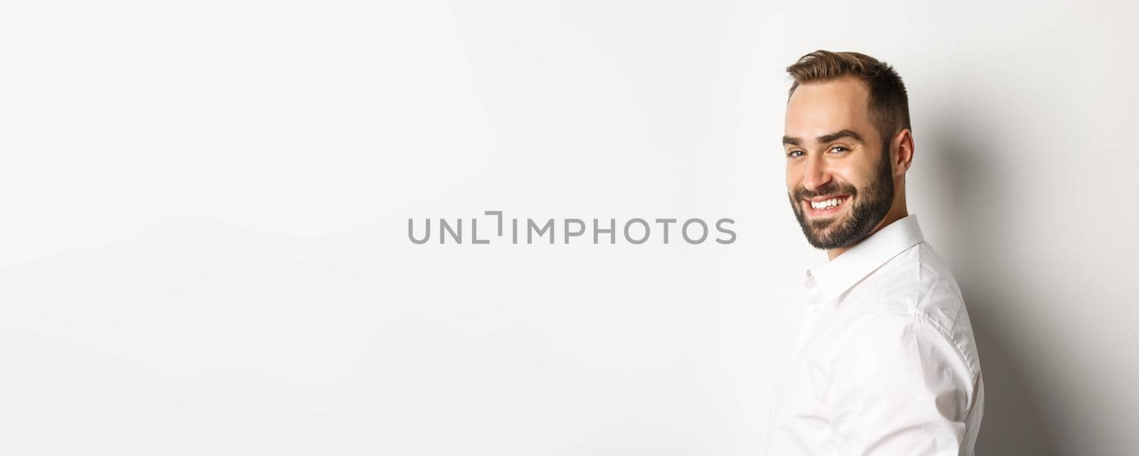 Close-up of confident businessman turn face at camera, smiling self-assured, standing over white background.