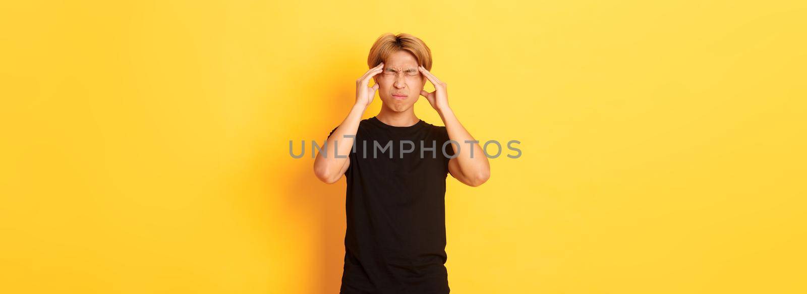 Portrait of troubled asian male student having headache, grimacing from pain and touching head, suffering migraine.