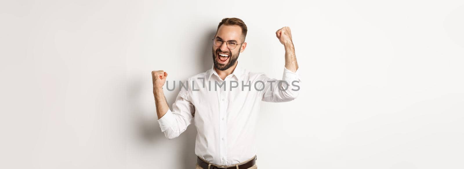 Successful businessman rejoicing, raising hands up and celebrating victory, winning something, standing over white background.