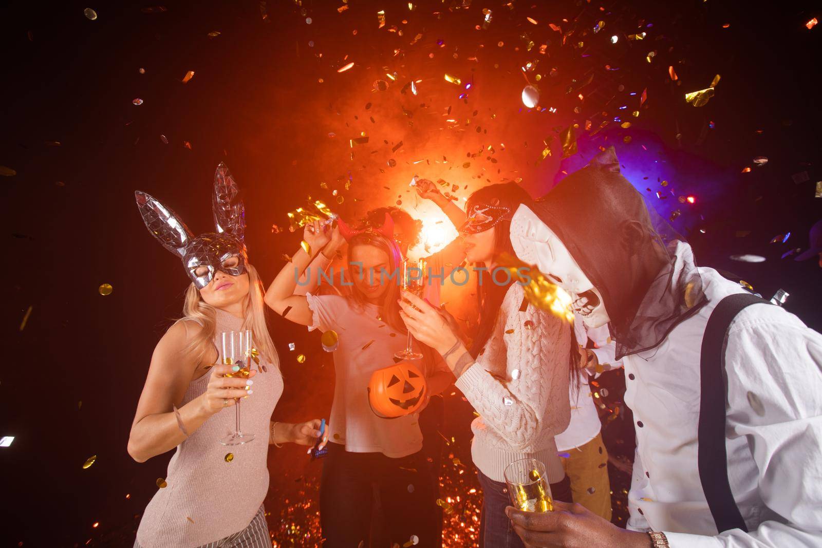 People dance at Halloween party with champagne glasses. Friends in the costumes in nightclub