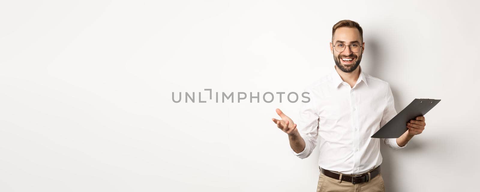 Handsome boss looking satisfied, holding clipboard and praising you, standing over white background.