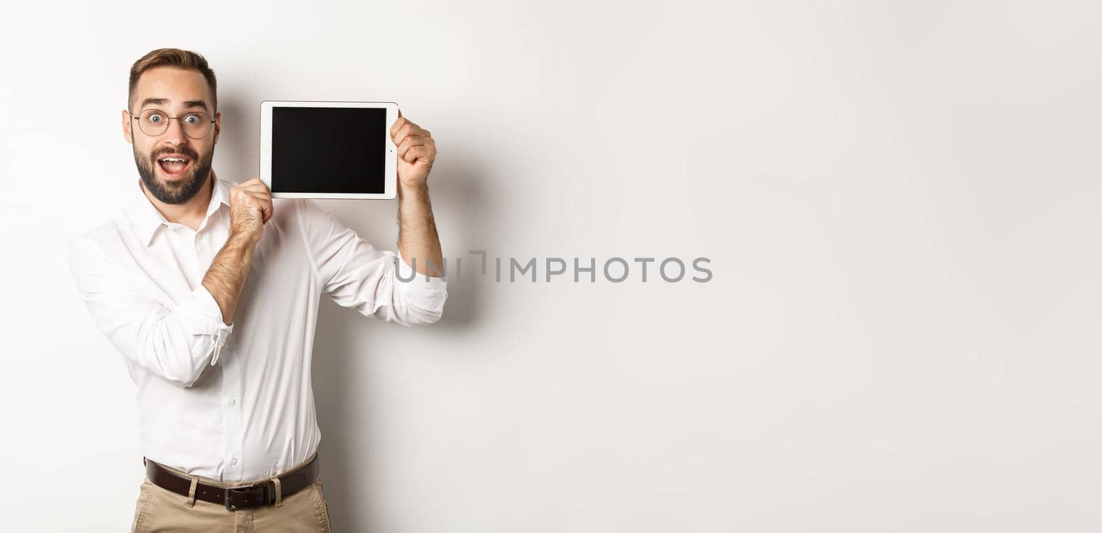 Shopping and technology. Handsome man showing digital tablet screen, wearing glasses with white collar shirt, studio background.