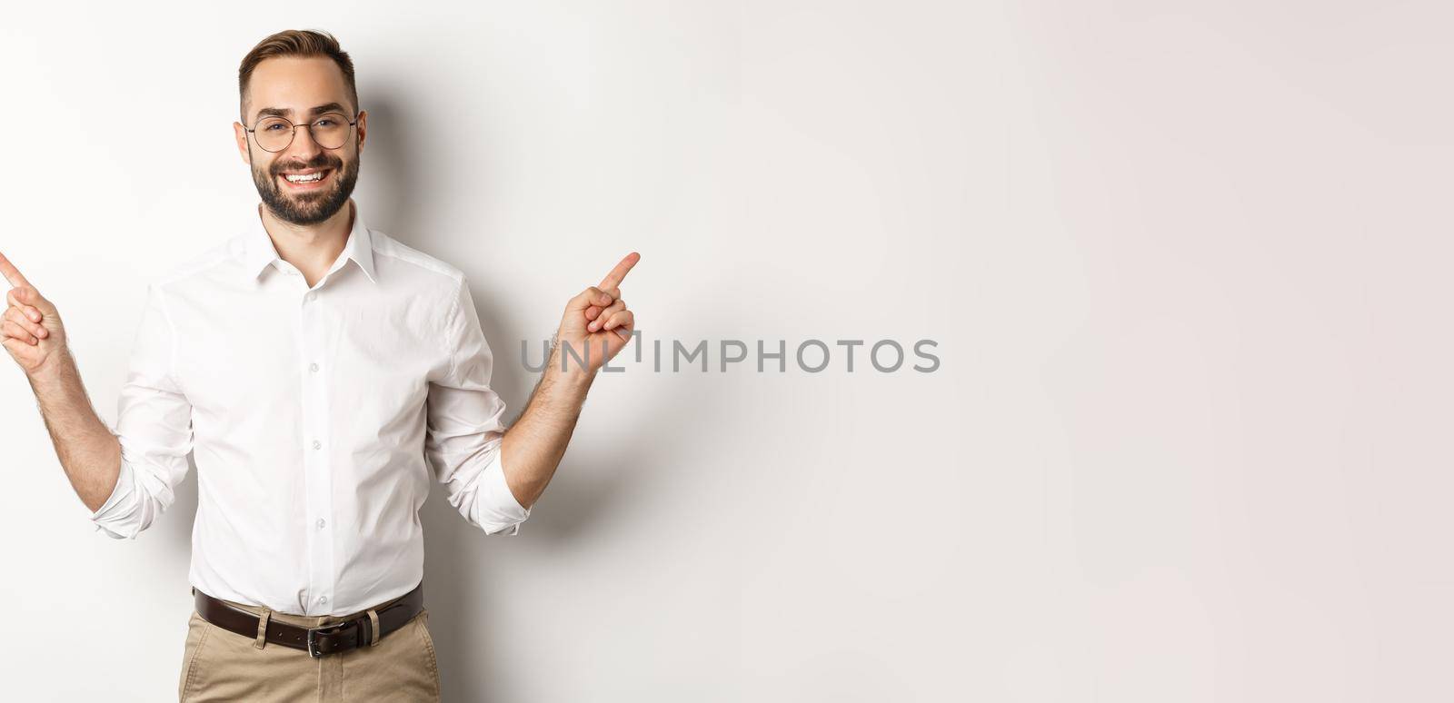 Confident bearded man smiling, pointing left and right at copy spaces, standing over white background by Benzoix