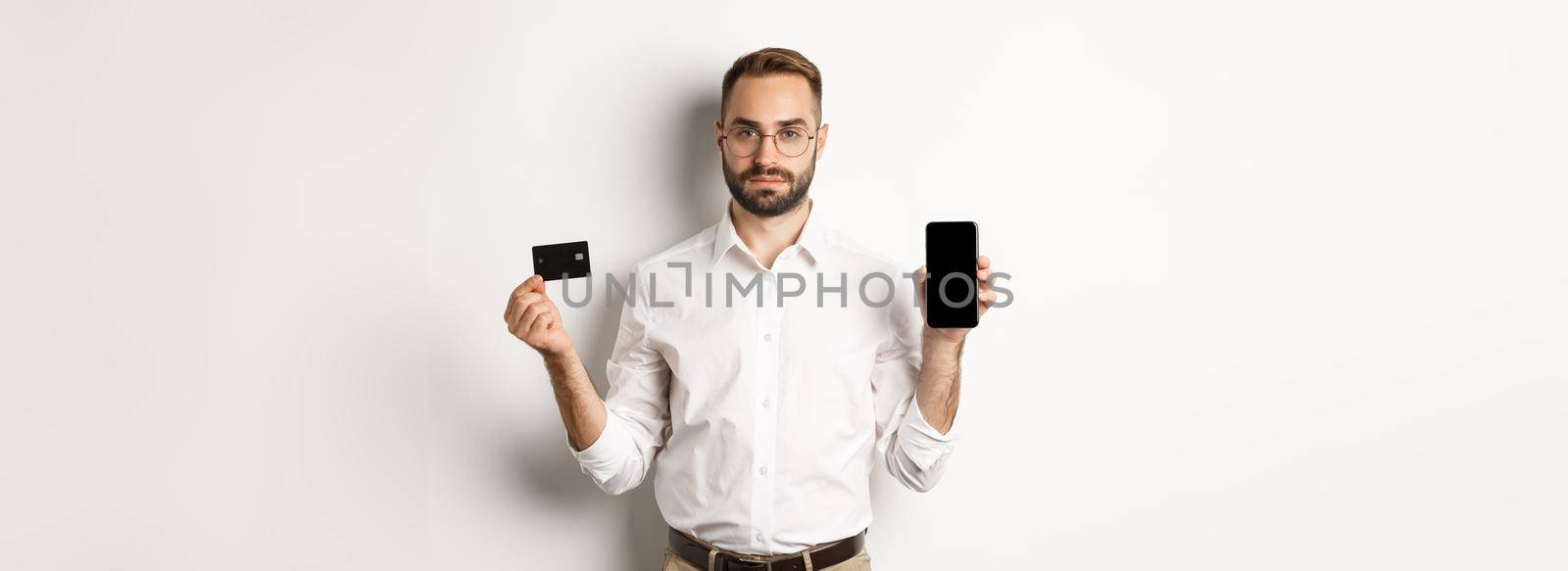 Serious business man showing mobile screen and credit card. Concept of online shopping.