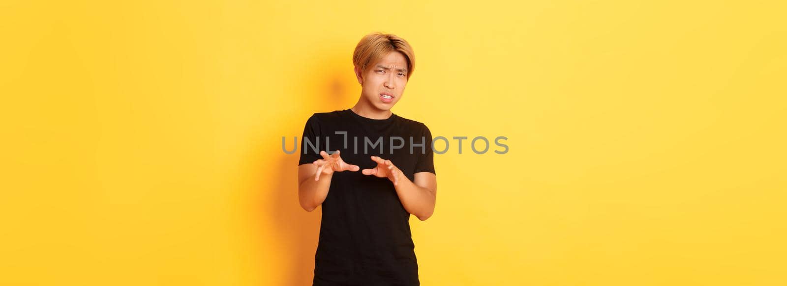 Portrait of disgusted picky asian guy, refusing and grimacing, standing yellow background.