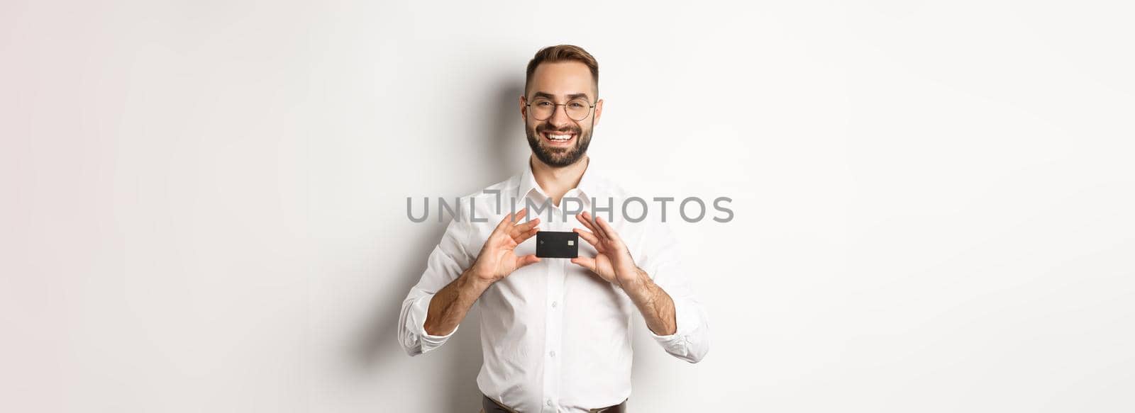 Handsome businessman holding a card, smiling satisfied, standing over white background by Benzoix