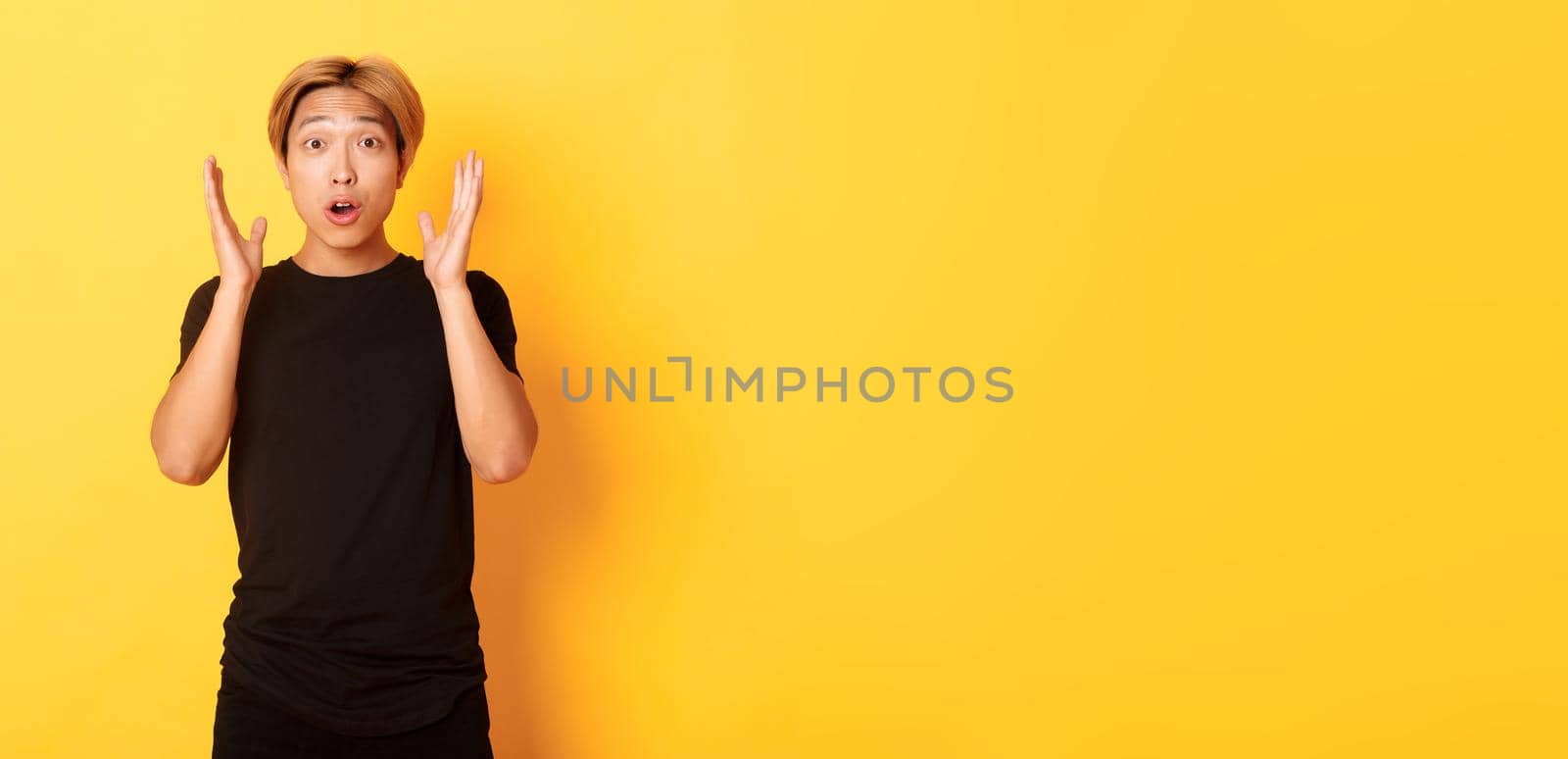 Portrait of surprised gasping blond asian guy reacting to awesome news, yellow background.