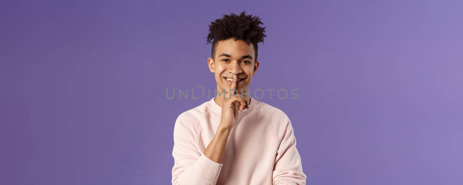 Close-up portrait of attractive smiling young man hiding secret, asking keep silent or quiet to do surprise, show shush gesture, place index finger to mouth, standing purple background by Benzoix