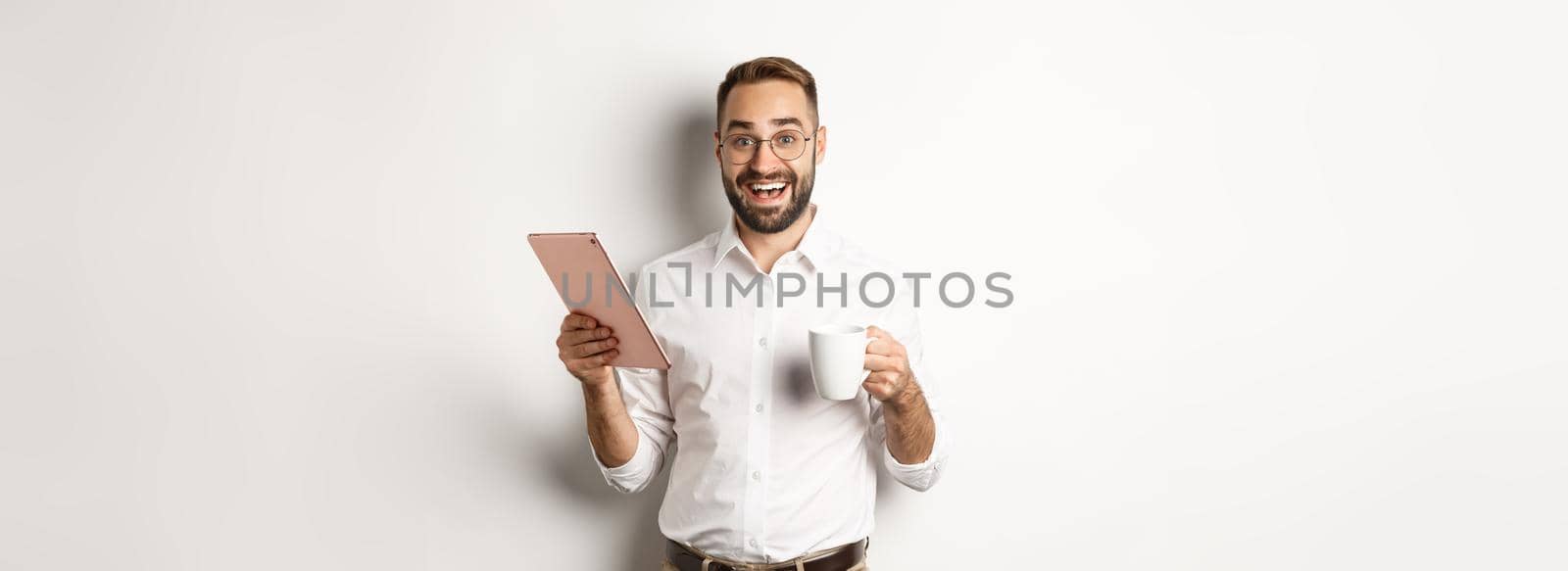 Excited manager reading on digital tablet, working and drinking coffee, standing against white background by Benzoix