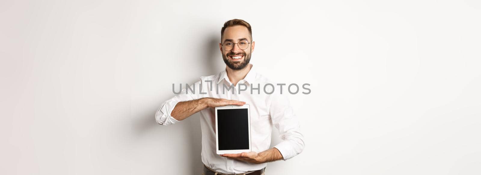 Smiling manager showing something on digital tablet screen, demonstrating website, standing over white background.