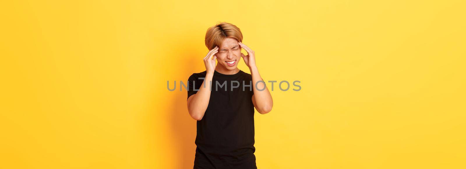 Portrait of troubled asian male student having headache, grimacing from pain and touching head, suffering migraine by Benzoix