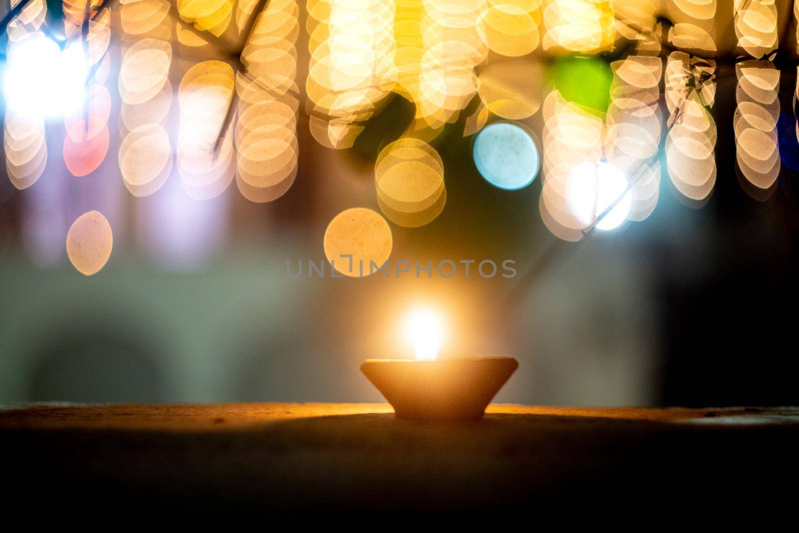 lone earthenware oil lamp diya set against colorful bokeh balls showing the lighting and decoration during the hindu festival of diwali showing a serene peaceful vision in the night by Shalinimathur