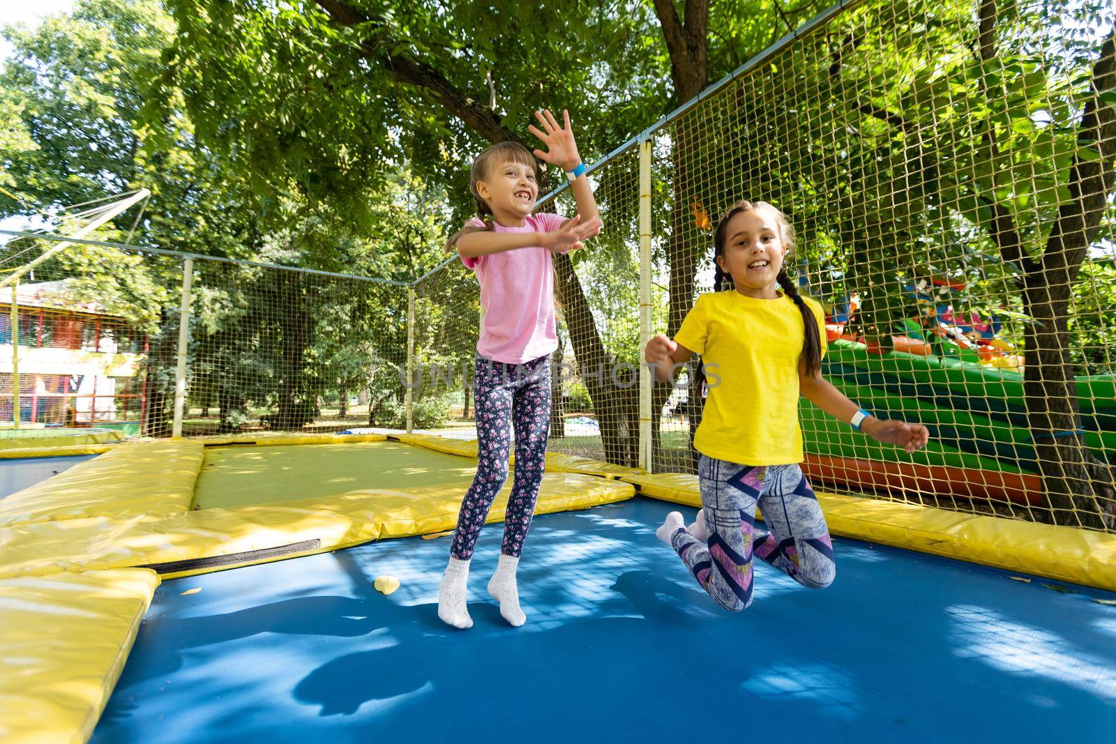 Two little girls in the summer jump on a trampoline, smiling and laughing. Children play. Relax in the fresh air. Friends jump on a trampoline. Happy child.