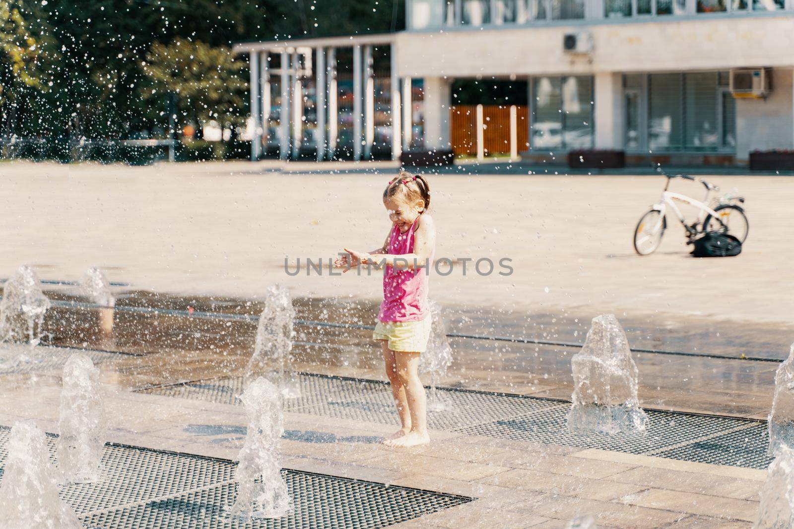 little girl playing with small fountains on the urban plaza