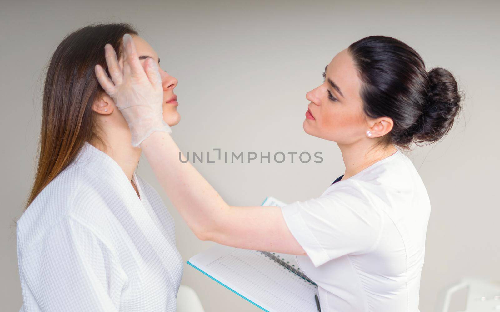 Curing skin problems. female cosmetologist looking at client's face through magnifying lamp examining her skin.