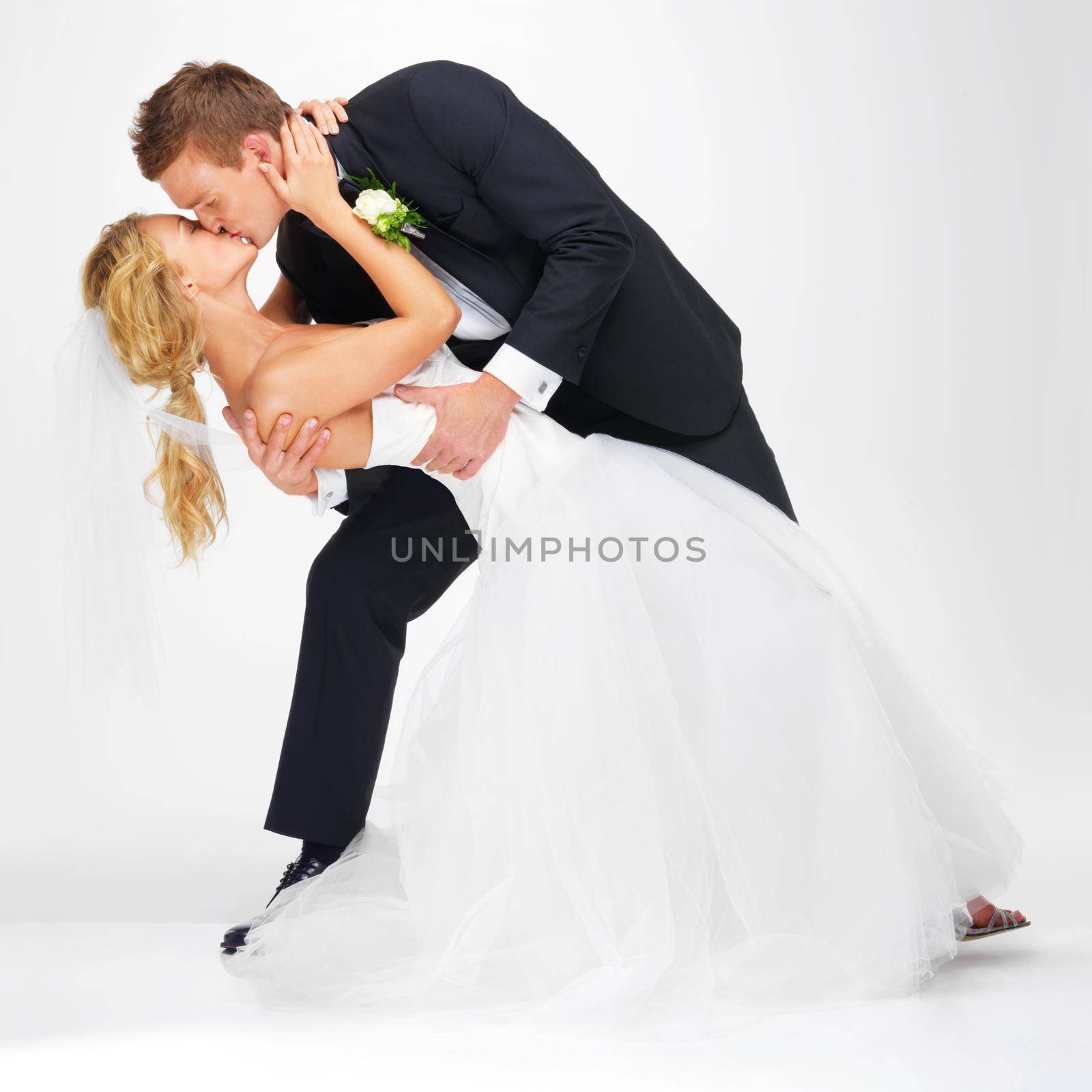 Wedding, couple and love with a kissing man and woman after marriage in studio on a white background. Young bride and groom at a celebration event together, happy and romantic in a dress and suit by YuriArcurs