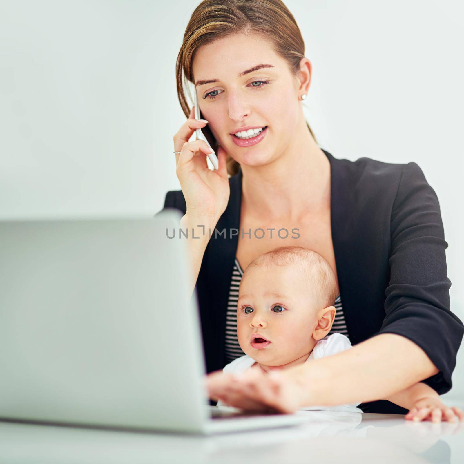 Growing a career and a family. a successful young businesswoman looking after her baby boy while working on her laptop and phone. by YuriArcurs