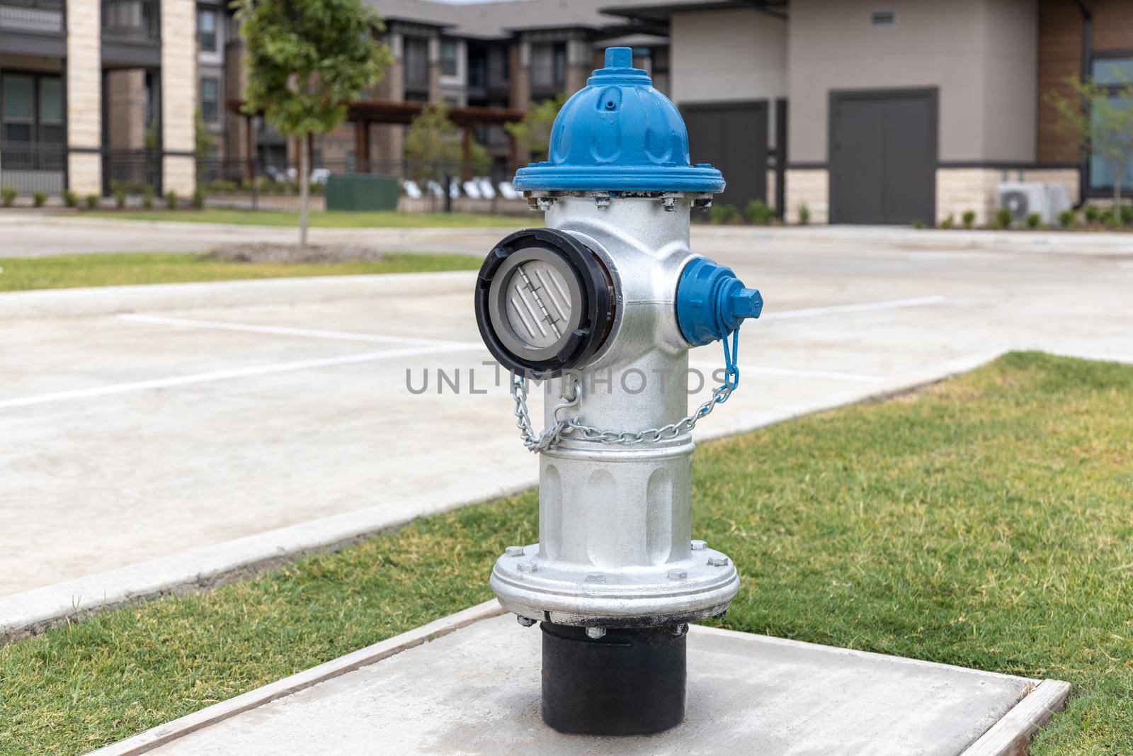 Grey and blue fire hydrant on sidewalk in the yard in residential complex with asphalt road and building on background